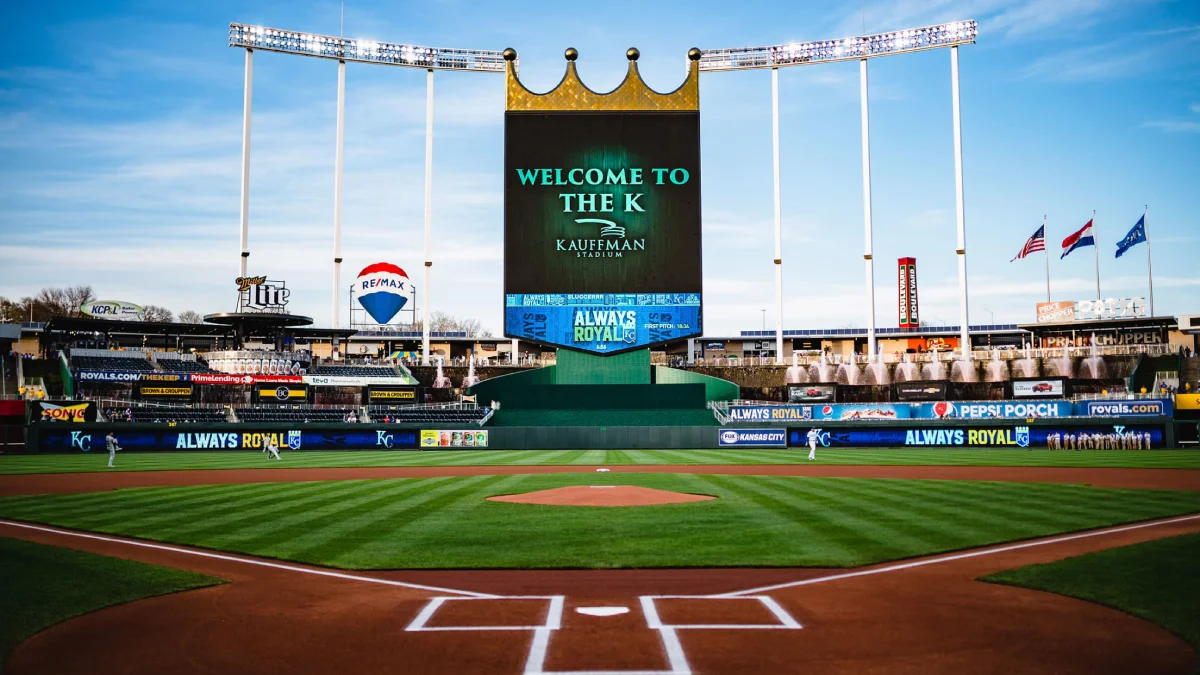 The expansive, lush green baseball field viewed from home plate with the large scoreboard and towering light fixtures vi