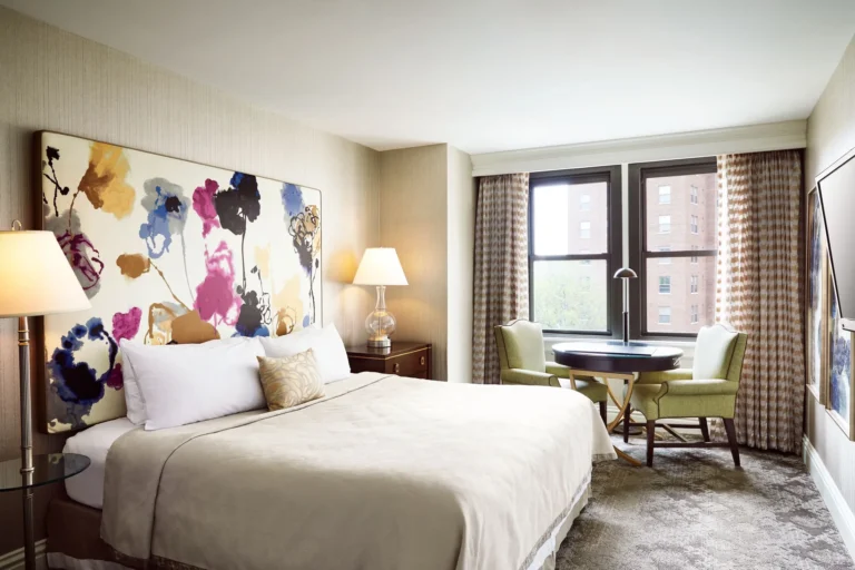 A luxurious hotel queen room featuring a vibrant floral art headboard, white linens, and a comfortable seating area next