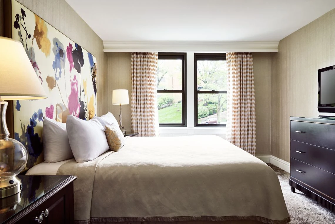A luxurious boutique hotel room featuring a king size bed, vibrant watercolor floral headboard, and a bright window over