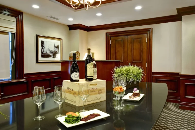 An elegant hotel event space with dark wood trim, featuring a table set for wine tasting with appetizers, wine glasses,
