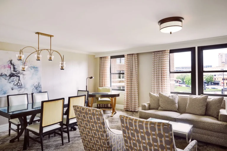 View of a luxurious hotel suite living area with abstract art, modern chandelier, a dining set, and comfortable seating