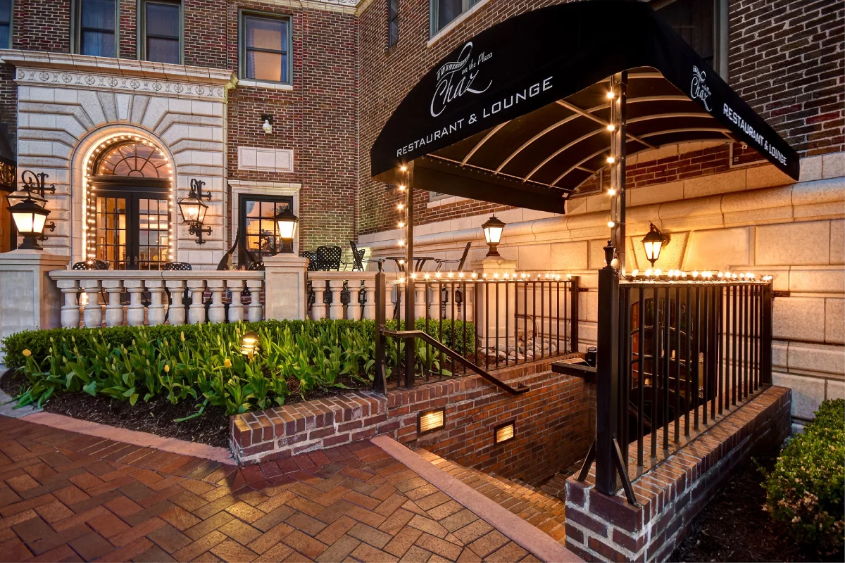 The illuminated entrance of a luxury restaurant and lounge at a historic Kansas City hotel, featuring brickwork, stone a