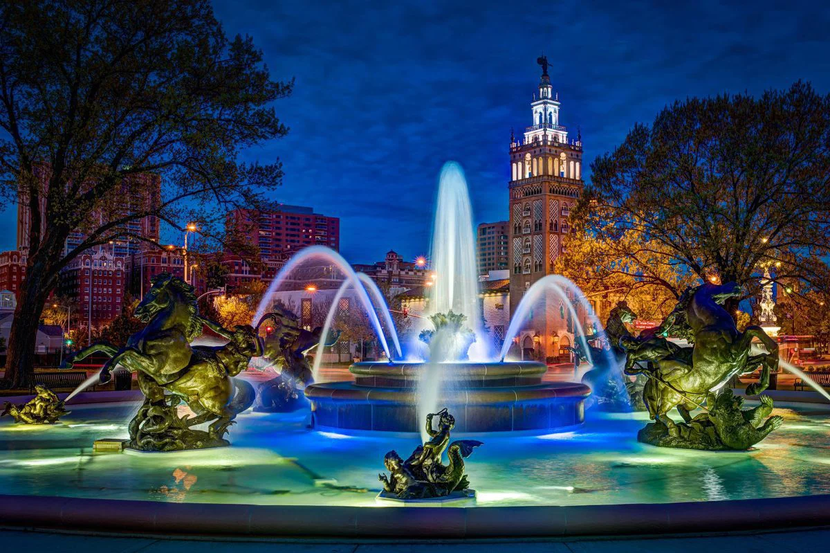 The J.C. Nichols Memorial Fountain glowing blue at twilight with bronze statues and the Country Club Plaza tower visible