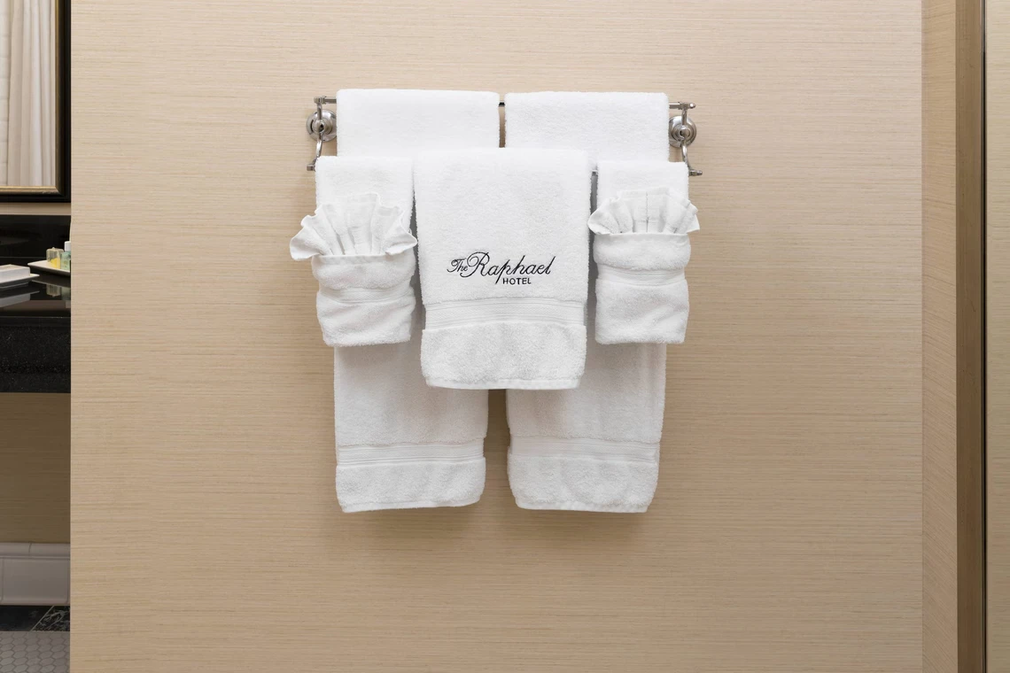 Intricately folded white luxury hotel towels hang neatly on a towel bar in a high-end Kansas City hotel bathroom.