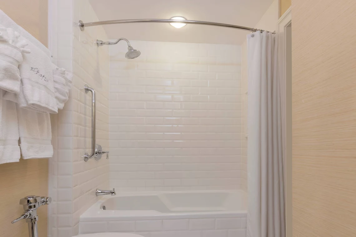 A modern hotel bathroom featuring white subway tile walls, a tub/shower combination, polished chrome fixtures, and a sta