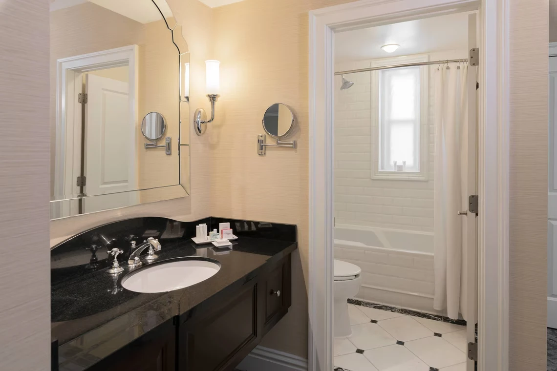 The elegant hotel bathroom features a black granite vanity countertop, chrome fixtures, and a separate bathtub area with