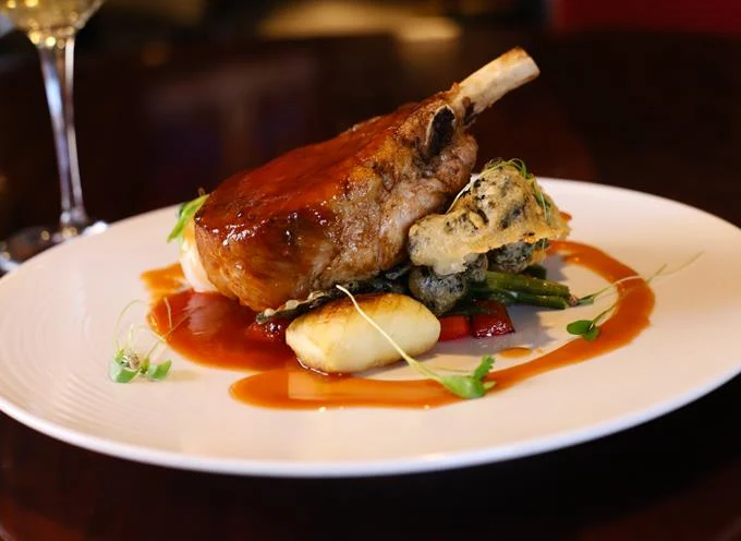 A beautifully plated glazed bone-in pork chop with vegetables and orange sauce, featured at Chaz Restaurant and Lounge, a romantic Kansis City restaurant.