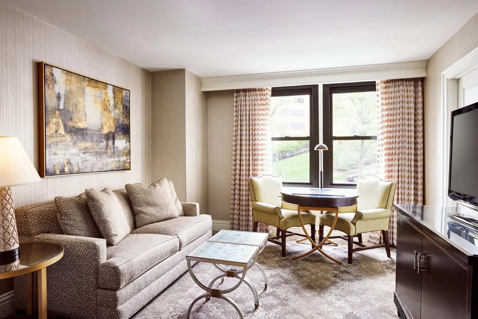 A luxurious hotel suite sitting area featuring a comfortable beige sofa, a coffee table, and two chairs.